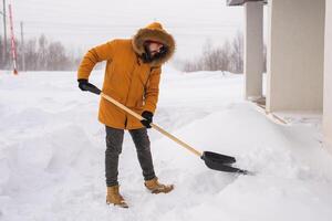 A man cleans and clears the snow in front of the house on frosty day. Cleaning the street from snow on a winter day. Snowfall and severe snowstorm in winter. photo
