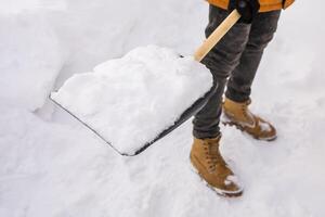Close-up man cleaning snow from sidewalk and using snow shovel. Winter season photo