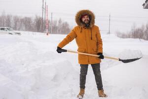 A man cleans and clears the snow in front of the house on frosty day. Cleaning the street from snow on a winter day. Snowfall and severe snowstorm in winter. photo