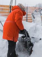 Red snow blower in action. Man outdoor in front of house using snowblower machine for removing snow on yard. Snow thrower in winter outside home. Young worker guy blowing snow photo