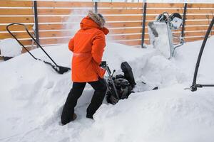 Red snow blower in action. Man outdoor in front of house using snowblower machine for removing snow on yard. Snow thrower in winter outside home. Young worker guy blowing snow photo