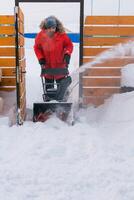 Red snow blower in action. Man outdoor in front of house using snowblower machine for removing snow on yard. Snow thrower in winter outside home. Young worker guy blowing snow photo