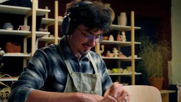Male potter sculpting clay modeling in ceramics studio handmade hobby Caucasian smiling carefree happy man guy artist designer creating crockery handcraft listen music headphones in pottery workshop video