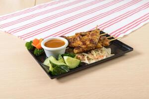A plate with a bowl of sauce and a skewered chicken photo
