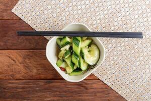A bowl of cucumber and chopsticks on a table photo