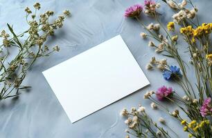 White blank card surrounded by colorful wildflowers on a light textured background photo