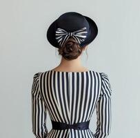 Elegant woman in a striped dress and wide-brimmed hat posing against a light background photo