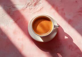 Warm cup of coffee resting on pink surface with soft shadows in the afternoon light photo