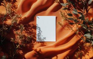 Blank canvas on textured orange fabric surrounded by greenery and soft shadows in natural light photo