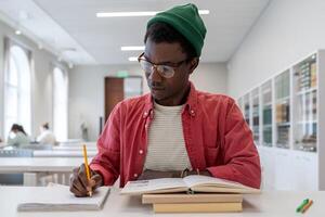 Focused african american guy college student sitting at desk with textbooks, studying in library photo