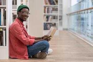 Smiling Black student man reading book in university library , looking at camera. Reading hobby. photo