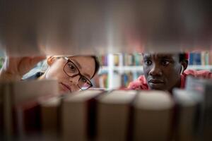 Two diverse students searching sources for research project in university library photo