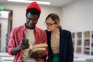 Two diverse students standing in classroom using smartphone during study break photo