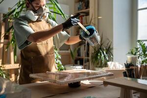 Concentrated woman, liquid artist creating pattern on canvas while working with epoxy resin painting photo