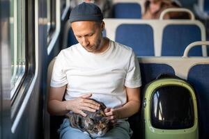 Cat owner traveling in electric train gentle touching pet lying on lap. Trip with domestic animals. photo