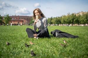 Pensive woman savoring ice cream in waffle cone, sitting on grass in park while lost in thought photo