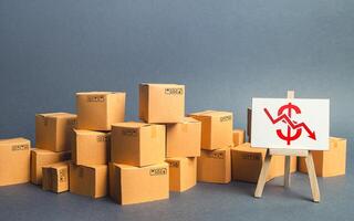 Lot of goods cardboard boxes and easel with a red dollar down arrow. Decline trade production rates, decreased sales. Low export. Economic reduced, industry degradation. Marketing, price reduction. photo