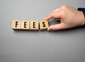 Fees word concept. Fixed price charged for a specific service. Business and finance concept. Costs, charges, commissions, penalties. Cost, fee and taxes. Wooden blocks photo