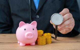 Businessman with stethoscope and piggy bank with coins. Financial health and well-being concept. Manage money wisely, ensure financial stability photo