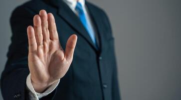 Businessman shows stop with his hand. Refusal, restriction, or caution. Bocking risks. Setting boundaries, rejecting offers. Business ethics, financial caution, or stopping negative trends. Leadership photo