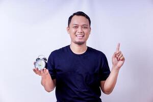 A smiling asian man holds an alarm clock pointing upward, signaling the importance of time management isolated on white background photo
