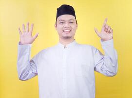 Smiling asian muslim man wearing casual clothes showing and pointing up with fingers number seven photo