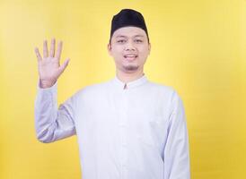 Smiling asian muslim man wearing casual clothes showing and pointing up with fingers number five photo