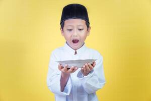 An asian boy looks enthusiastically at the plate in his hand, the concept of Ramdan Kareem celebration. photo