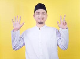 Smiling asian muslim man wearing casual clothes showing and pointing up with fingers number eight photo