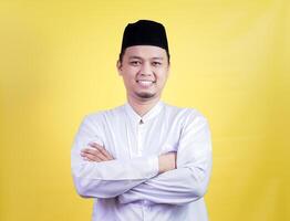 A smiling asian muslim man in a white outfit poses confidently against a yellow background photo