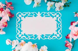Beautiful orchid flowers on light blue background with paper card note. Minimal concept. Creative spring and summer layout. Flower aesthetic with unique copy space. Flat lay, top of view. photo