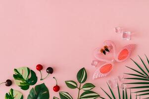 Trendy layout with tropical leaves, pink flamingo party sunglasses, ice cubes and red cherries on pastel pink background with copy space. Creative summer aesthetic concept. Beach party idea. Flat lay. photo