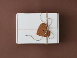 Present box with jute bow and heart shaped cookie on brown background. Minimal concept. Flat lay style. photo