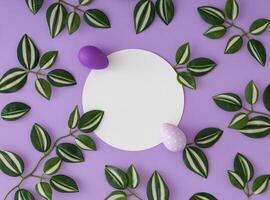 Spring pattern with green and white leaves and purple Easter eggs with paper card note copy space on purple background. Minimal creative Easter concept. Festive holiday flat lay idea. Top view. photo