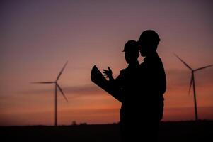 Silhouettes of two engineers standing and inspecting the operation of a wind turbine at sunset4 photo