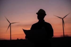 Silhouette of an engineer standing and inspecting the operation of a wind turbine at sunset.1 photo