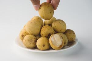 Hand Picking Fresh Langsat From a Plate with a Peeled Slice Showing photo