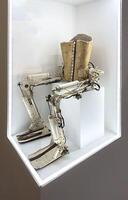 A vintage exoskeleton prosthetic designed for lower body mobility, featuring mechanical components, hydraulic systems, and a rigid torso support. Displayed in a minimalist illuminated case, this photo