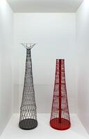 Two detailed scale models of radio towers, one black and one red, exhibited on a white pedestal in a minimalist gallery. The intricate lattice structures emphasize the technical and architectural photo