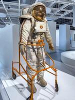 A detailed vintage Soviet-era space suit equipped with life support systems and a reflective visor. The suit features intricate details, including control mechanisms, a chest-mounted unit, and the photo