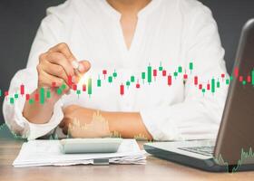 Businesswoman holding a pen pointing to graph stock on a virtual screen while sitting at the table in the office photo