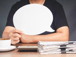 Close-up of a hand holding a blank white speech bubble while sitting at the table in the office photo