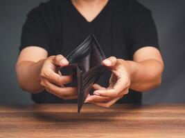 A young man opens an empty wallet while sitting at the table photo