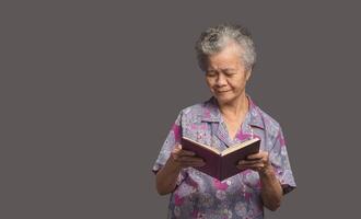 Elderly Asian woman read a book with a smile while standing on a gray background photo