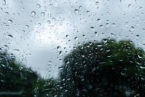 Raindrops on car window with cloudy sky and trees in the background photo