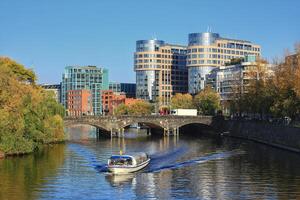 Berlin canal with boat passing by modern office buildings and bridge - Moabiter Brucke - on a sunny autumn day photo