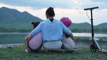 Mother and children sit and rest after riding scooters in the park. Mother and daughters spend their free time riding scooters outdoors together. Happy Loving Family. video