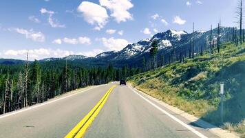 There is snow on the tops of the California mountains, and there is a road and car ahead. A view of the landscape of mountains and the road from the window of the POV car video
