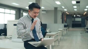An Asian man is using laptop computer , video calling to business partner in office
