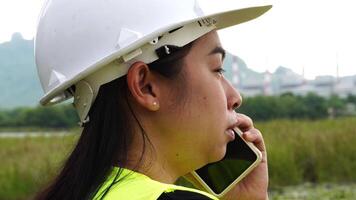 Female environmental engineer uses a smartphone near a reservoir against a power plant and high-voltage poles in the background. Energy, ecology and environment concept video